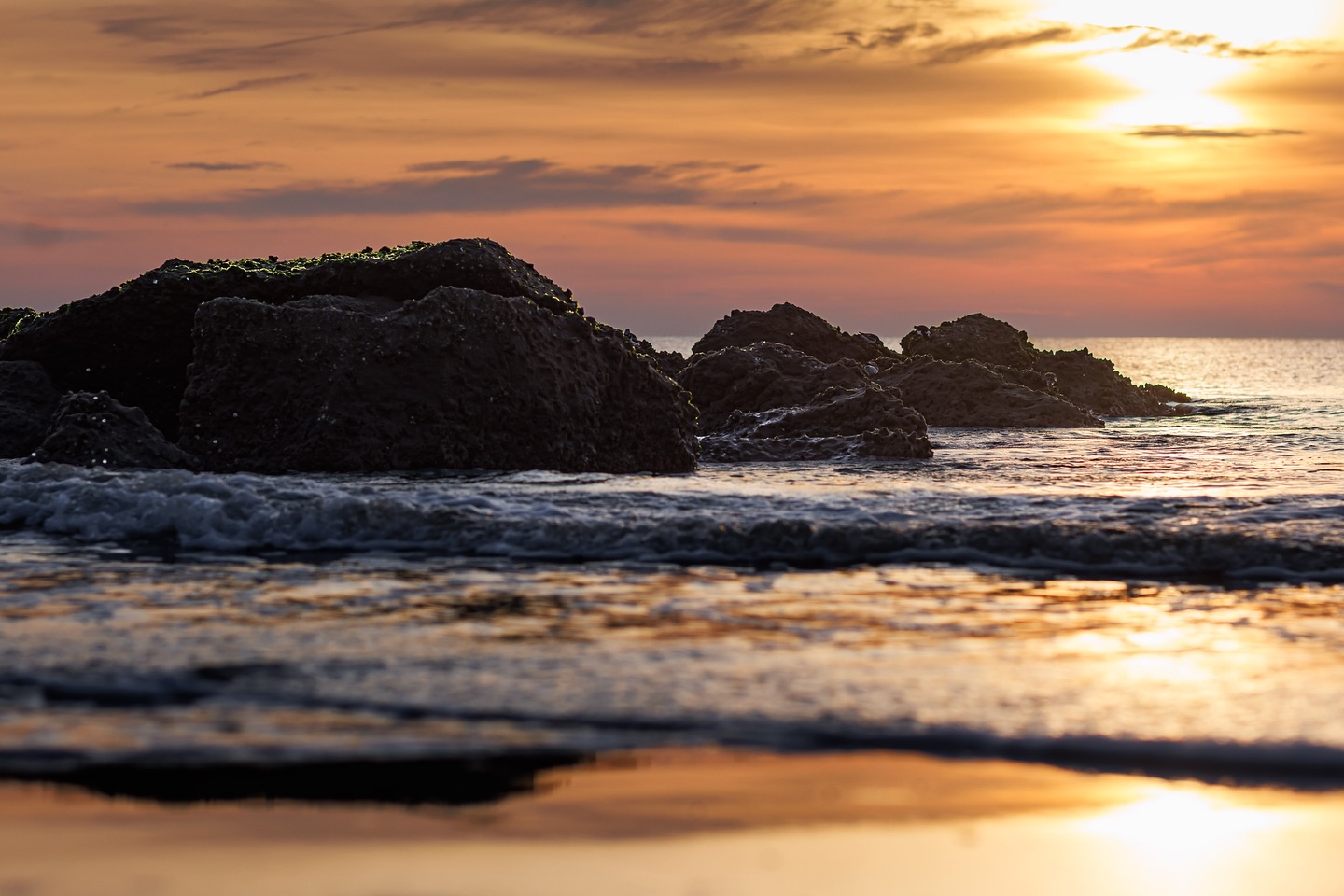 Boulders in the ocean at sunset on the beach.