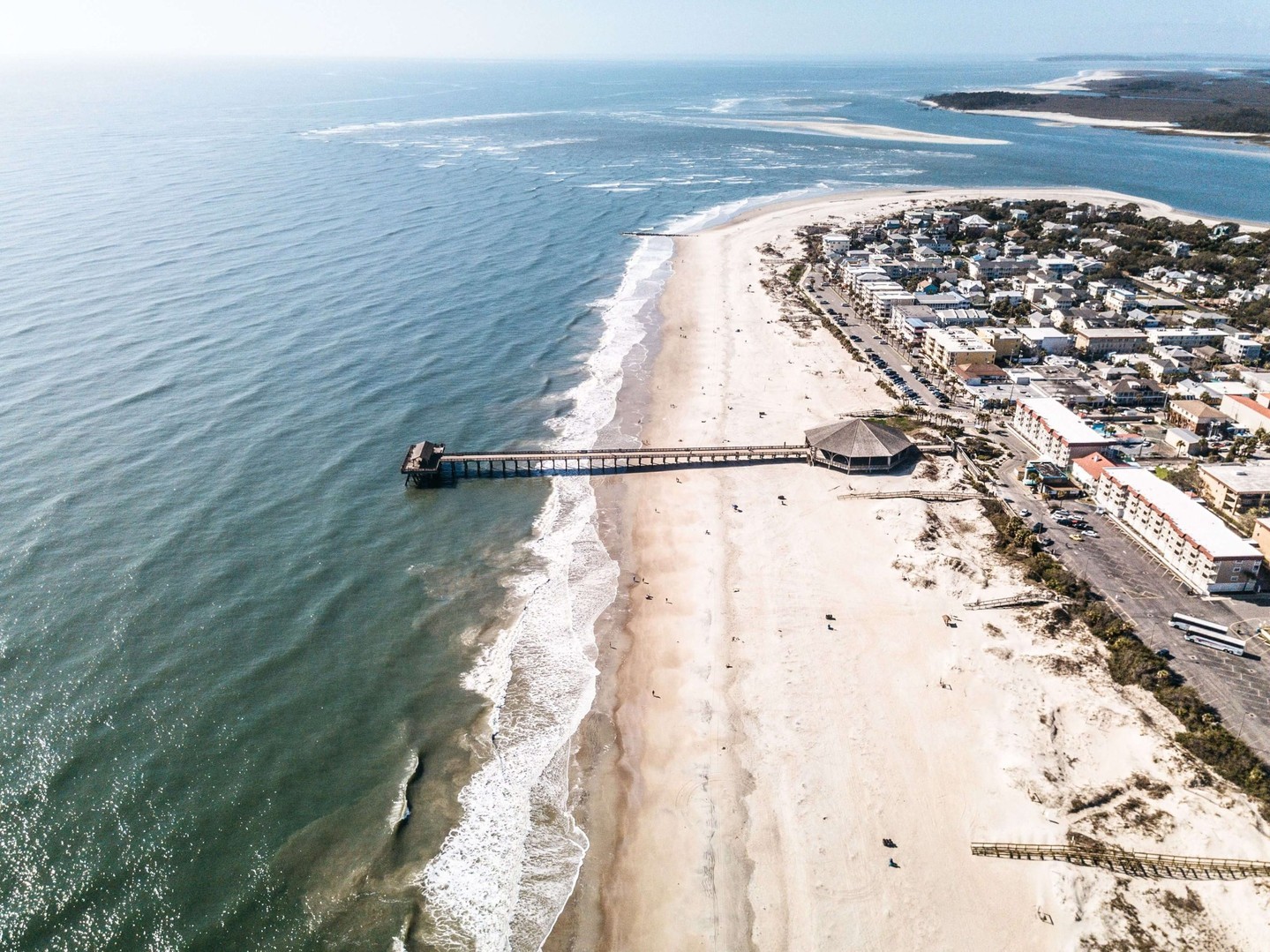 Aerial view of Tybee Island’s shoreline and pier, with sandy beaches, rolling ocean waves and coastal buildings lining the beachfront.