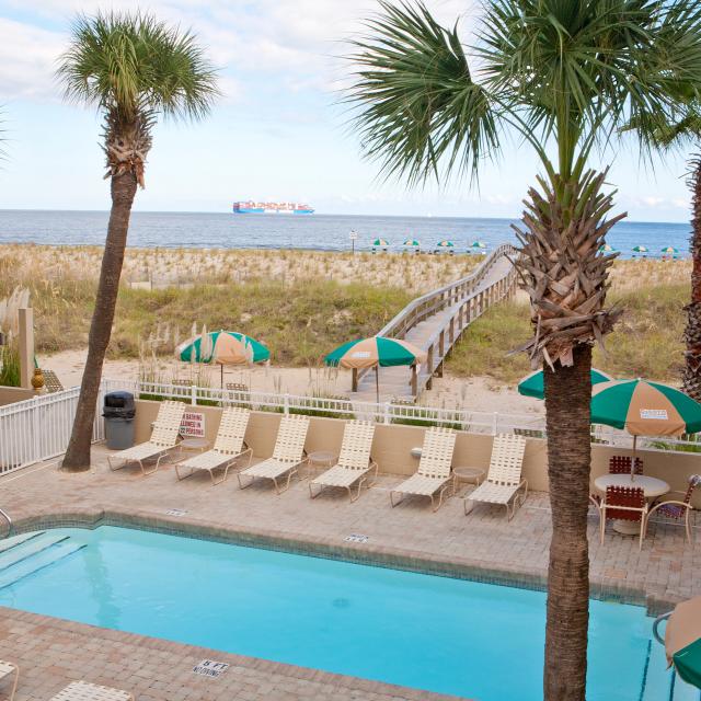 An outdoor pool view with seating, umbrellas and an oceanfront view