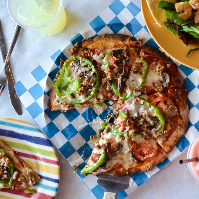 A pizza, shrimp salad and drink on a table.