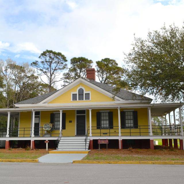 A front entrance outdoor view of a yellow historic guard house.