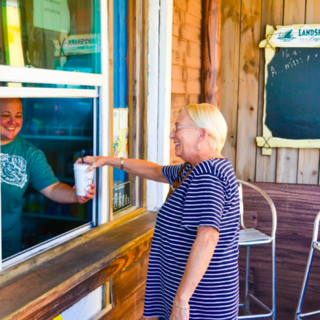 A woman grabbing a drink at an outdoor dining window on the beach.