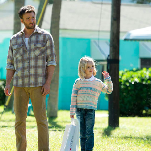 A man walks with a young girl who is waving towards someone not in scene.