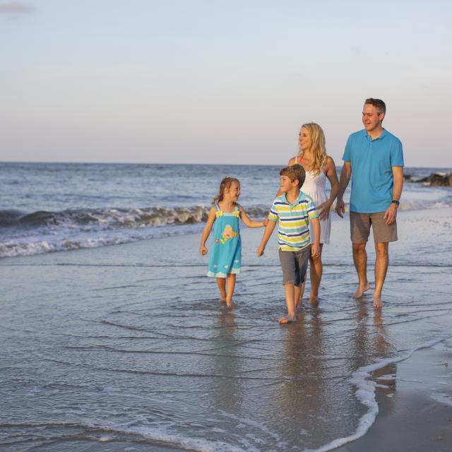 A family of four walking the beach as waves softly hit the shore
