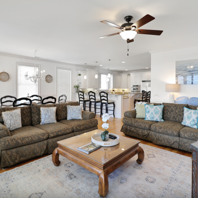 Large living room with white walls, two couches, coffee table, rug and ceiling fan