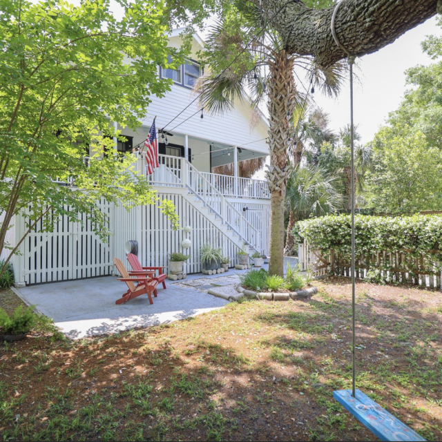 White vacation home; outdoor view of the property with a tree swing and red chairs.
