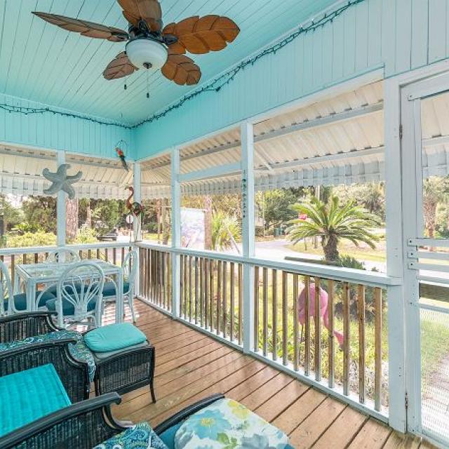 A screened in porch with seafoam green cushioned furniture.