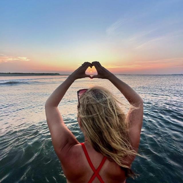 woman holding her hands up in a heart at sunset