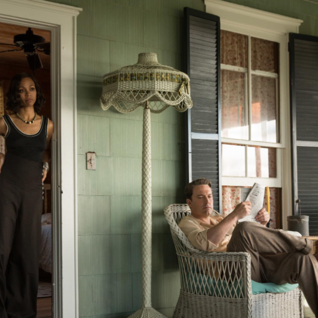 A man sitting on an outdoor porch and a woman standing in a doorframe.