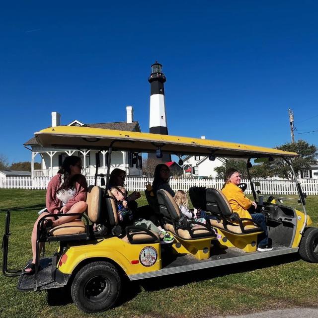 A small group on a golf cart tour with a lighthouse in the background.