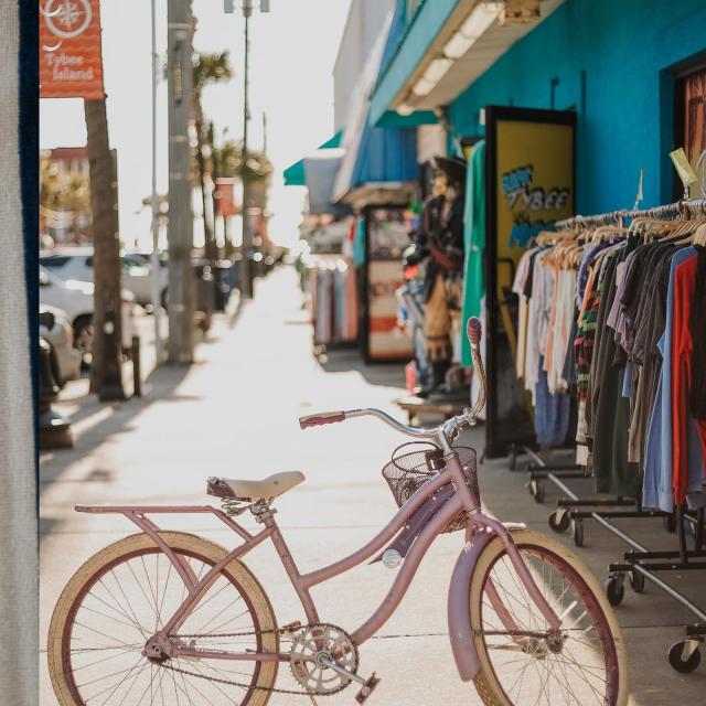A pink bike parked on a sidewalk near shops.