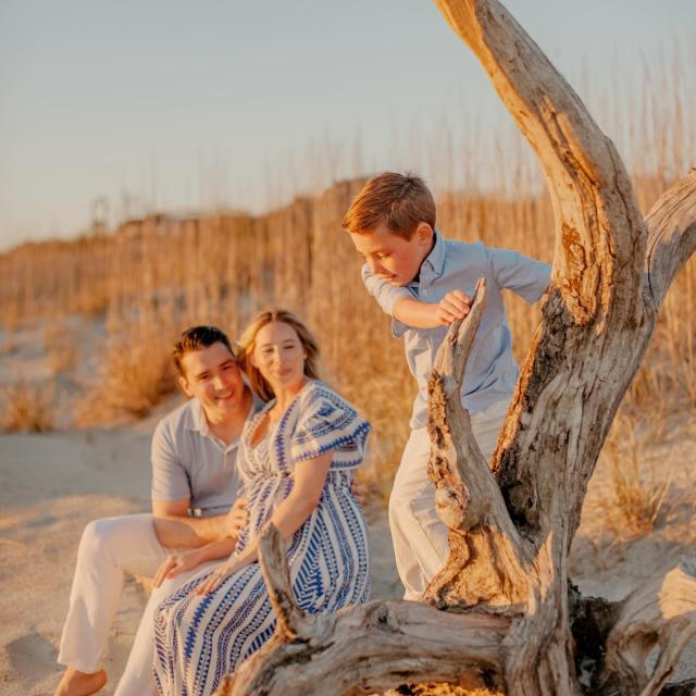 A couple sitting on the beach watching their young son play.