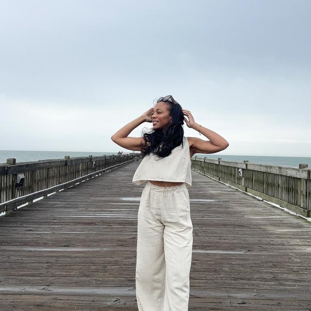 A woman standing on a beach boardwalk with the wind blowing her hair.