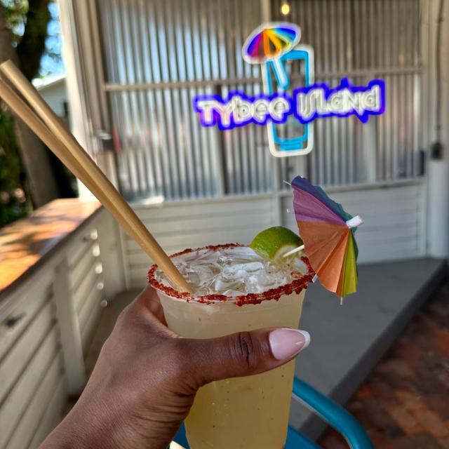 A person holding a drink with a small rainbow-colored umbrella.
