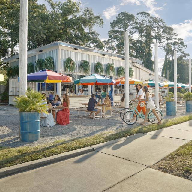 People eating outdoors at a restaurant with colorful rainbow umbrellas.