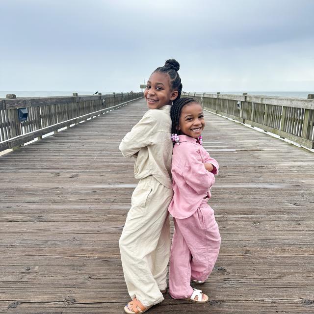 Two young children posing together on a dock at the beach.