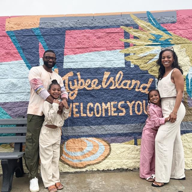 A family of four posing together in front of a wall mural sign that reads: Welcome to Tybee Island.