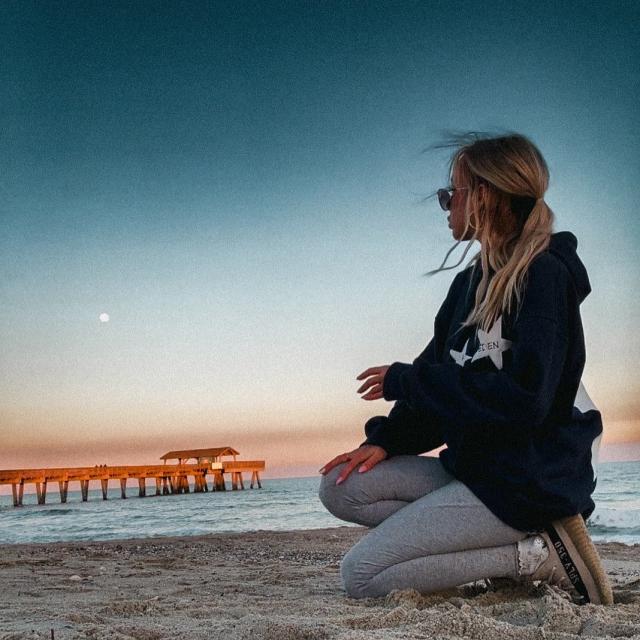 A woman kneeling in sand on the beach watchig the sun set.