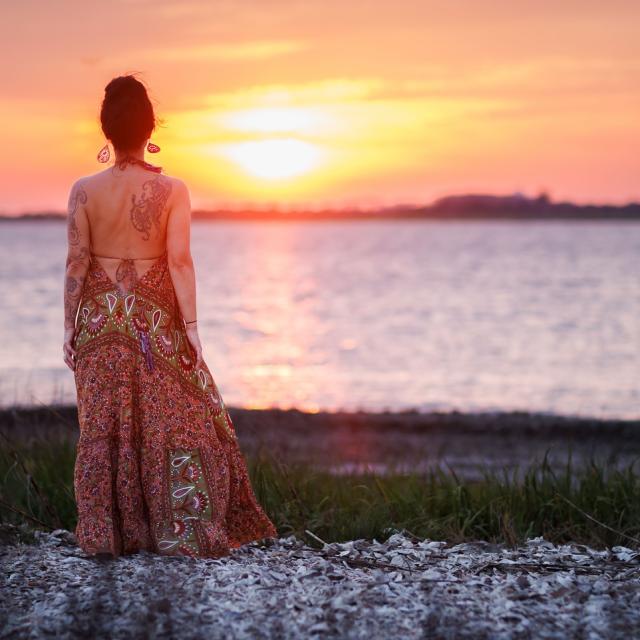 A woman standing on the beach watching the sunset.
