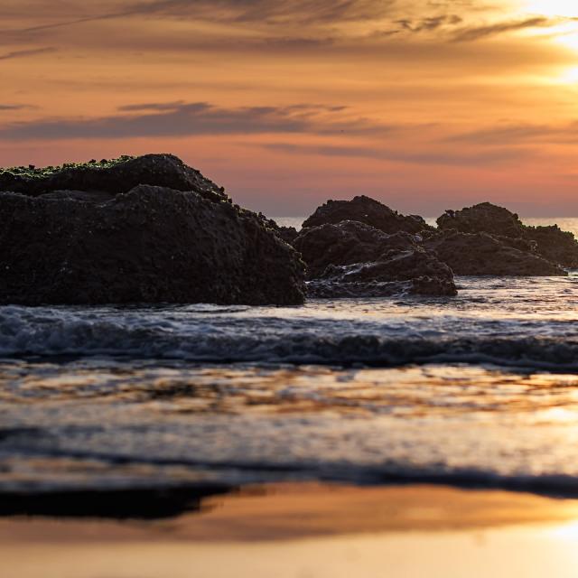 Boulders in the ocean at sunset on the beach.