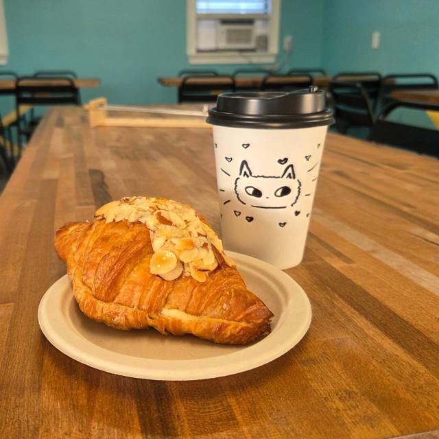 An almond croissant served on white plate with a to-go coffee.