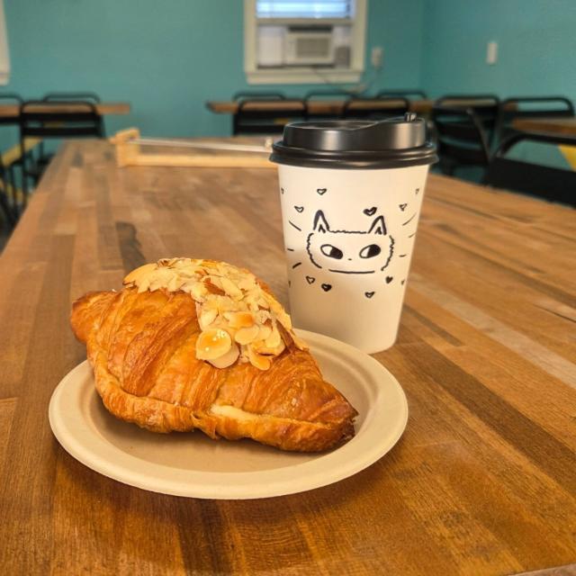 An almond croissant served on white plate with a to-go coffee.