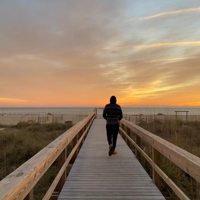 A man walking a boardwalk on the beach.