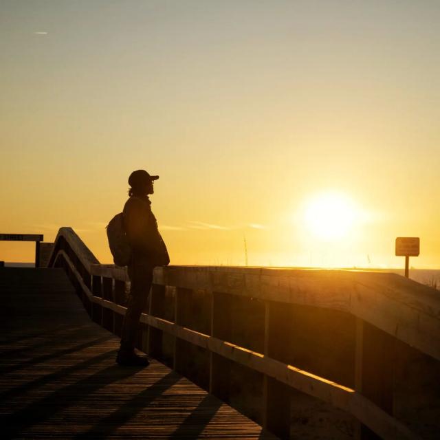 A man watching the sunset from the boardwalk on the beach.