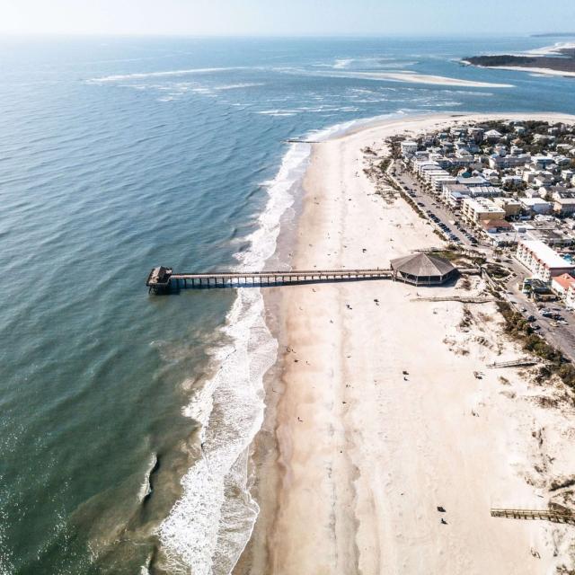 Aerial view of Tybee Island’s shoreline and pier, with sandy beaches, rolling ocean waves and coastal buildings lining the beachfront.