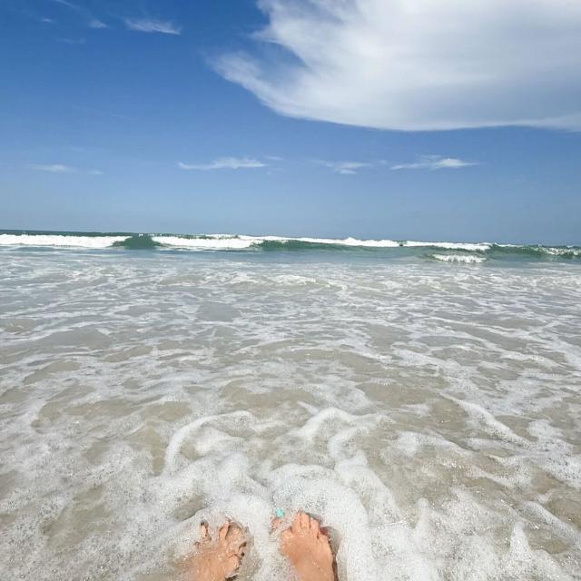 A person’s feet is washed by the ocean while sitting on the beach.
