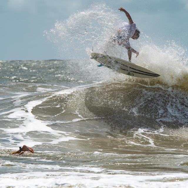 Surfer riding a breaking wave while another surfer paddles nearby.