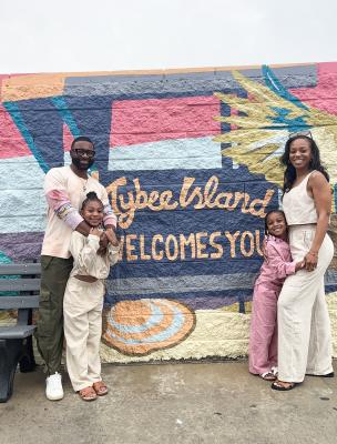 A family of four posing together in front of a wall mural sign that reads: Welcome to Tybee Island.
