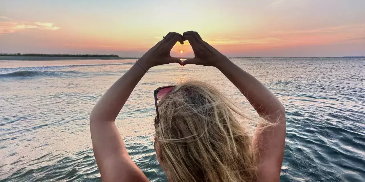 woman holding her hands up in a heart at sunset