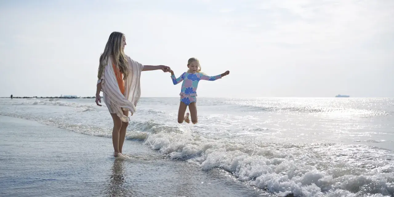 Mom and daughter on the beach playing in the ocean.