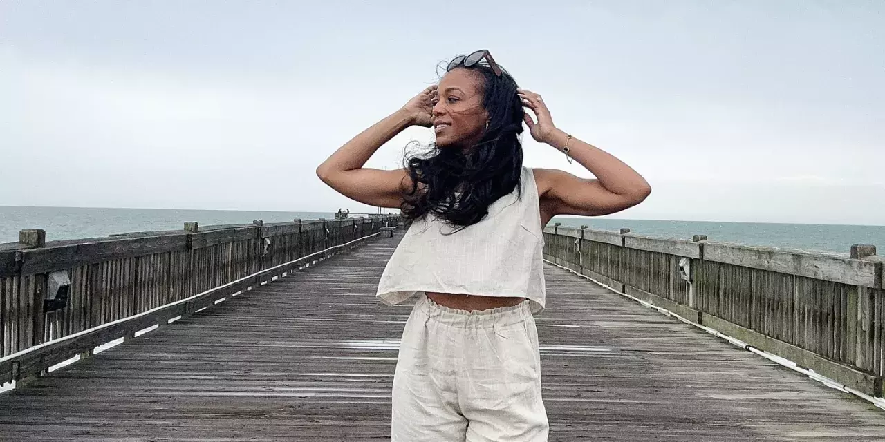 A woman standing on a beach boardwalk with the wind blowing her hair.