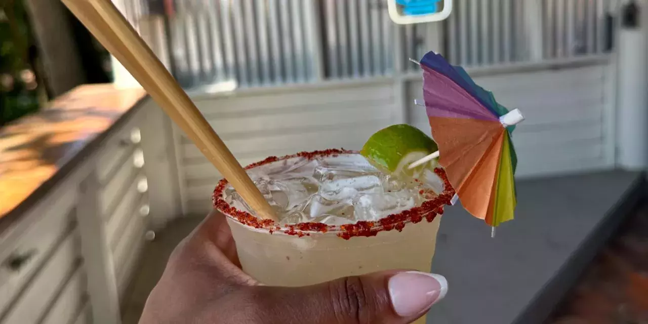 A person holding a drink with a small rainbow-colored umbrella.