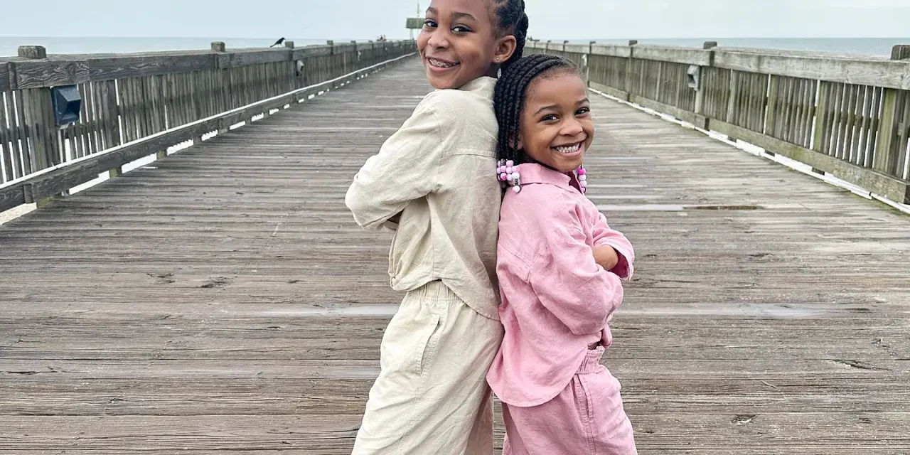 Two young children posing together on a dock at the beach.