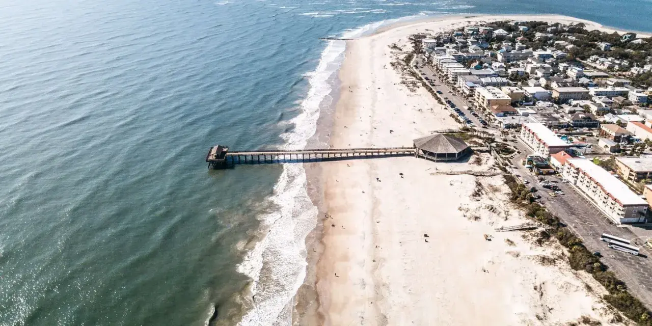 Aerial view of Tybee Island’s shoreline and pier, with sandy beaches, rolling ocean waves and coastal buildings lining the beachfront.