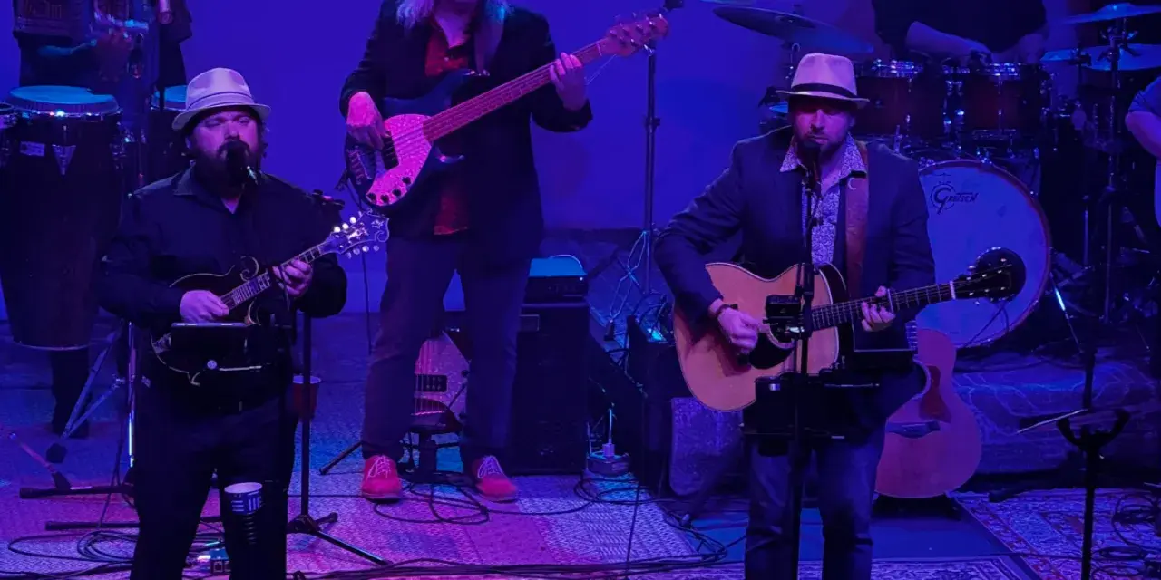 Five musicians performing on stage with guitars, bass and drums under purple and blue lighting.