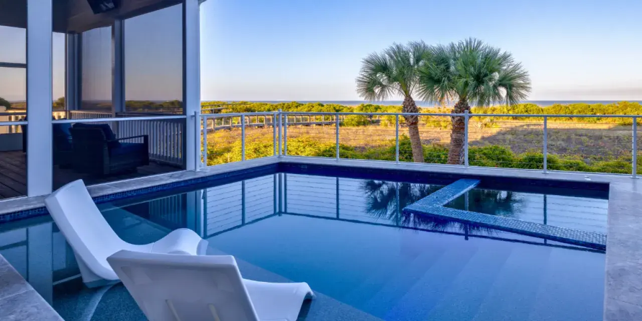 Private pool with in-water lounge chairs overlooking coastal dunes and palm trees on Tybee Island, with a screened porch and elevated deck seating.