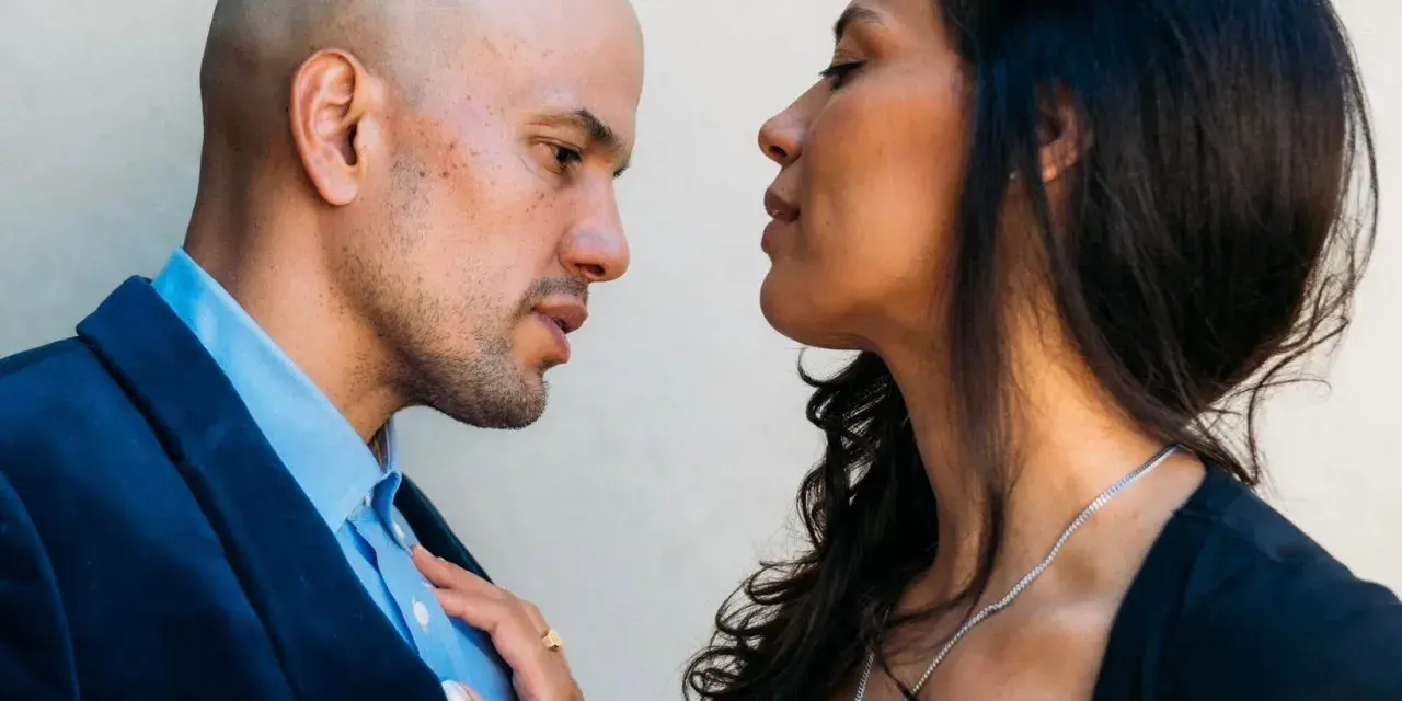 A couple facing one another. A woman resting her hand on the man’s chest.