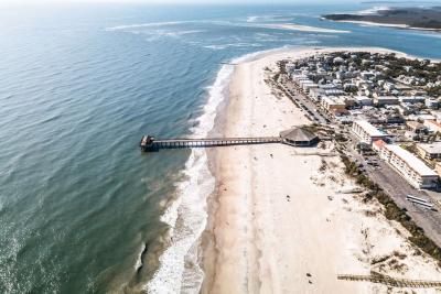 Aerial view of Tybee Island’s shoreline and pier, with sandy beaches, rolling ocean waves and coastal buildings lining the beachfront.