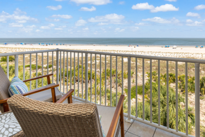 Oceanfront balcony view on Tybee Island with wicker seating overlooking sand dunes, beach and calm shoreline.