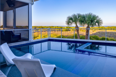 Private pool with in-water lounge chairs overlooking coastal dunes and palm trees on Tybee Island, with a screened porch and elevated deck seating.