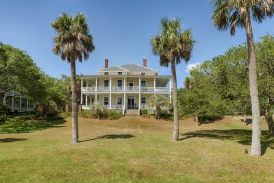 Historic Officer’s Row home on Tybee Island featuring wraparound porches, tall palm trees, expansive lawn and classic coastal architecture on the North End.