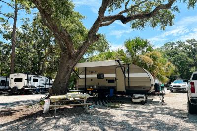 Travel trailer parked beneath a large shade tree at an RV site at River’s End Campground.