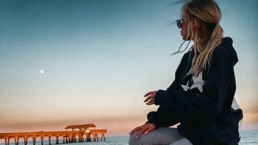 A woman kneeling in sand on the beach watchig the sun set.
