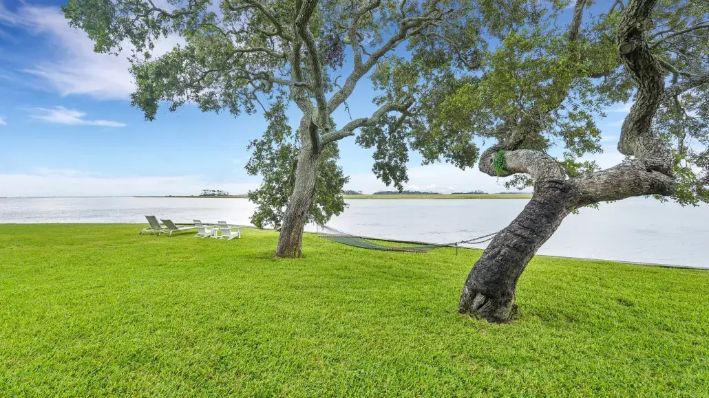 Waterfront lawn at Horsepen Cottage by Coastline Concierge, featuring live oak trees, a hammock and views of the tidal river.