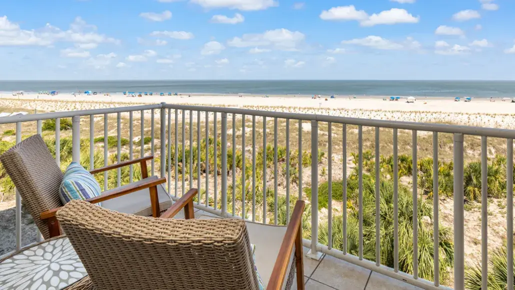 Oceanfront balcony view on Tybee Island with wicker seating overlooking sand dunes, beach and calm shoreline.