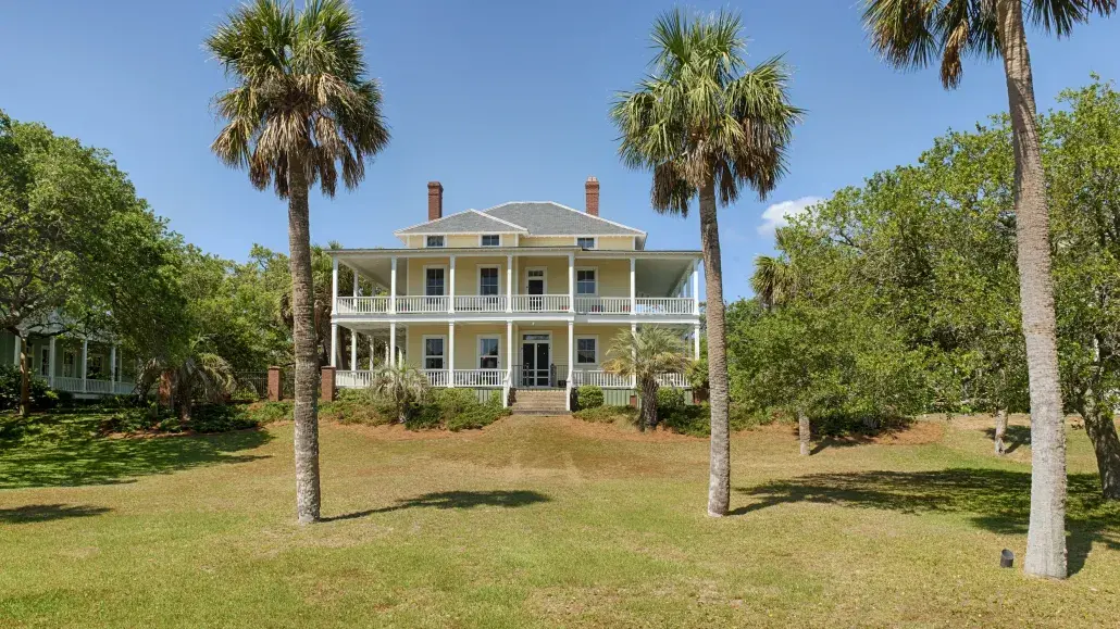 Historic Officer’s Row home on Tybee Island featuring wraparound porches, tall palm trees, expansive lawn and classic coastal architecture on the North End.